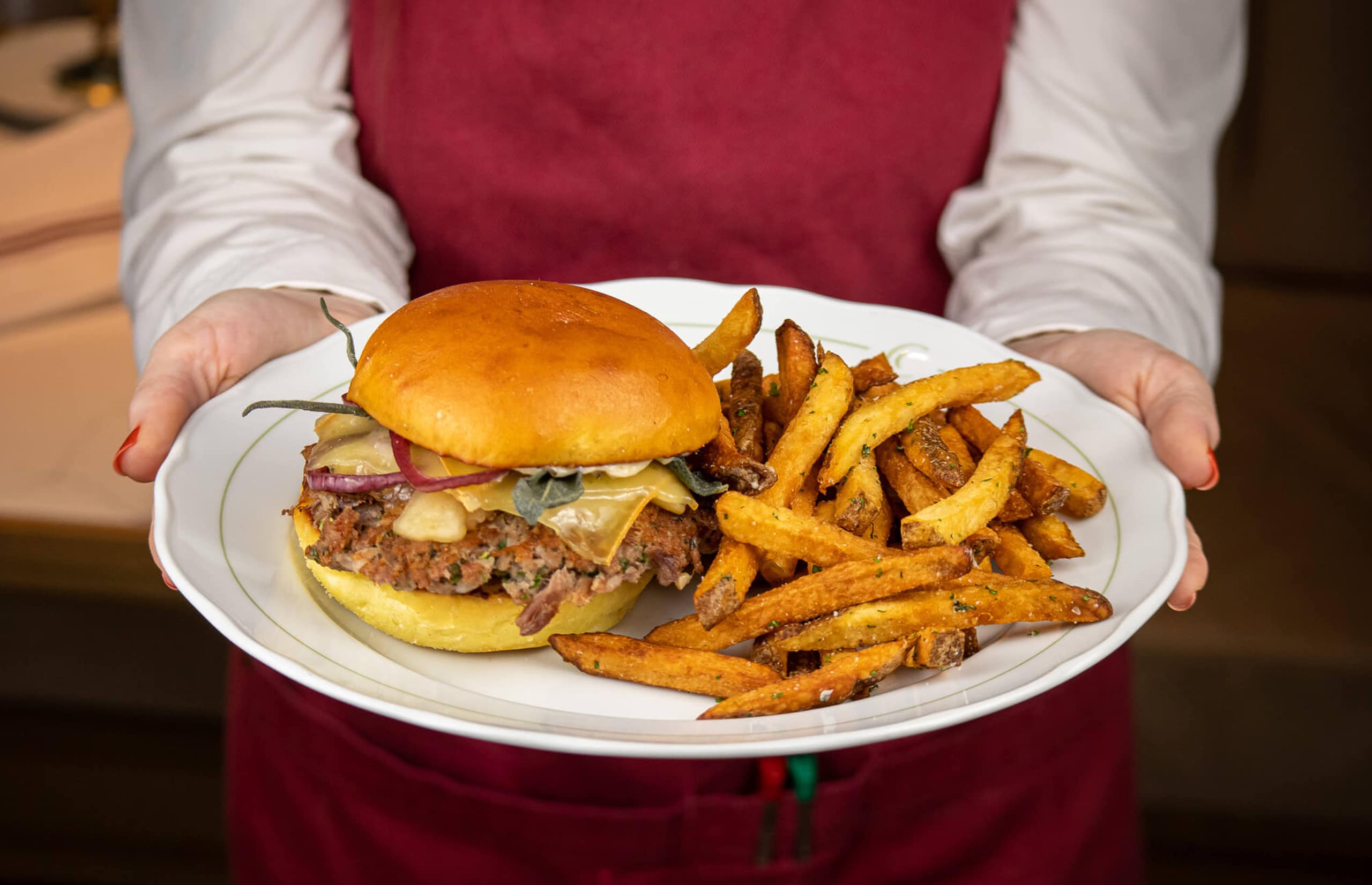 Server holding Cafe Lunette's Burger Bash burger on a white plate with fries
